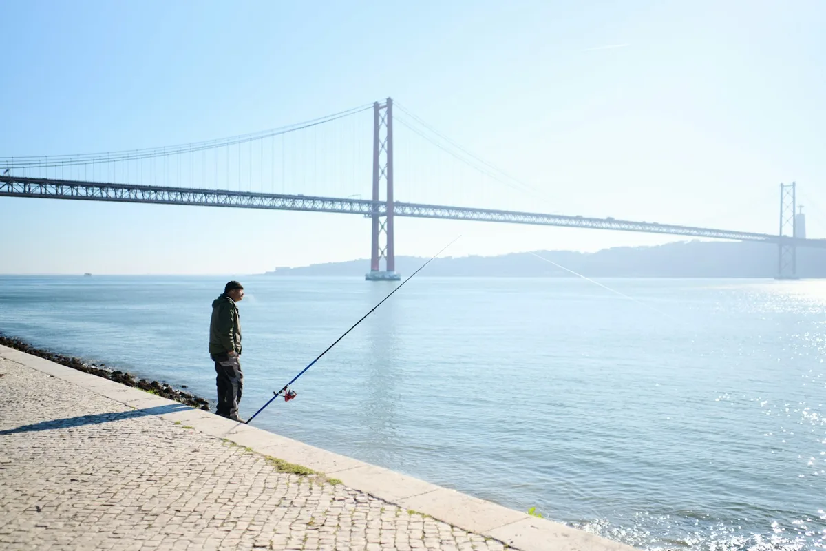 Pescador junto a um rio com uma ponte ao fundo