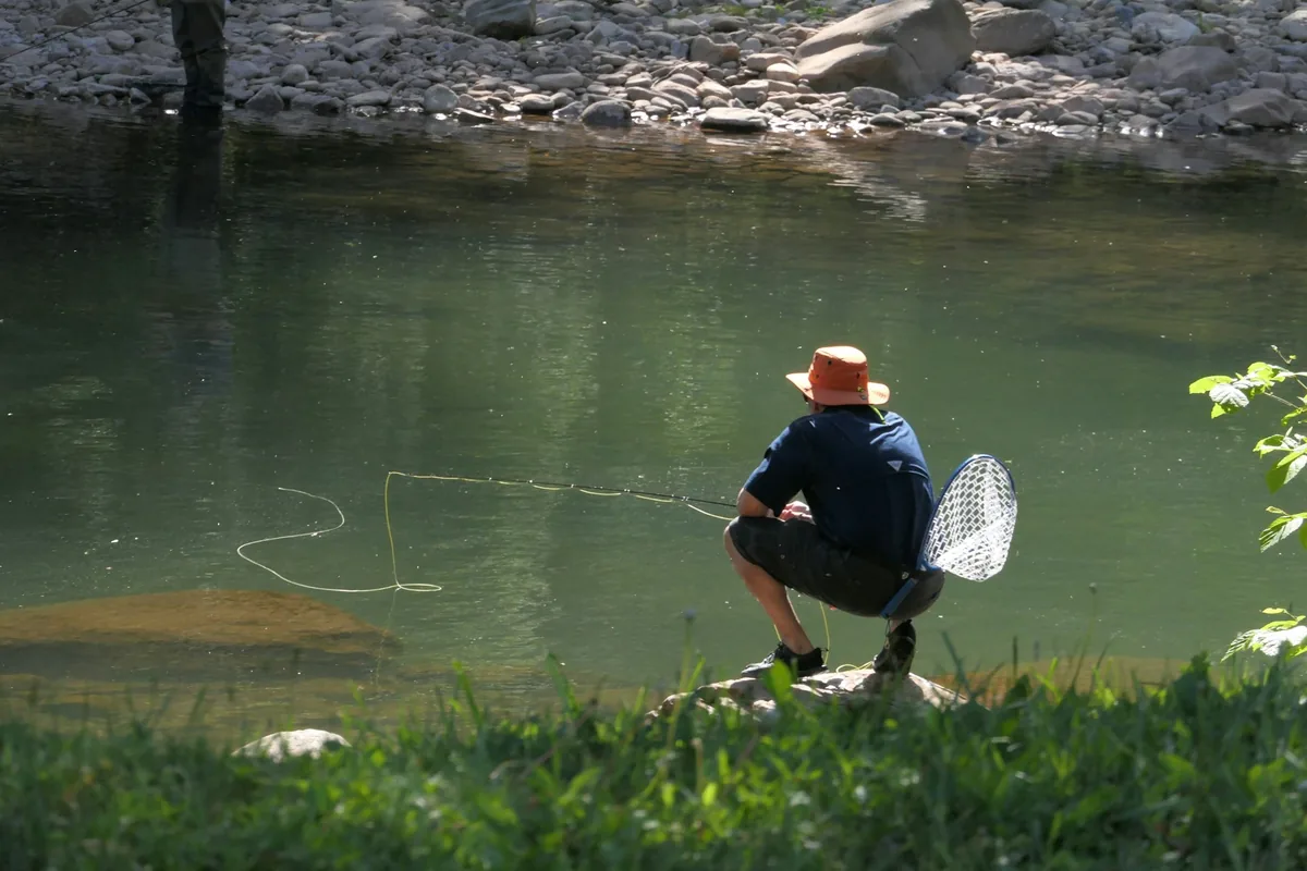 Pescador ajoelhado junto ao rio com camaroeiro na mão