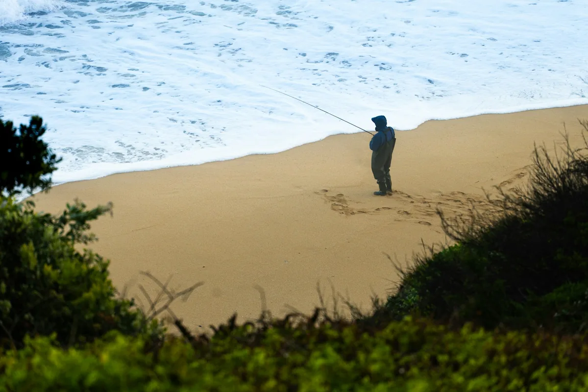 Pescador sozinho numa praia de areia com ondulação