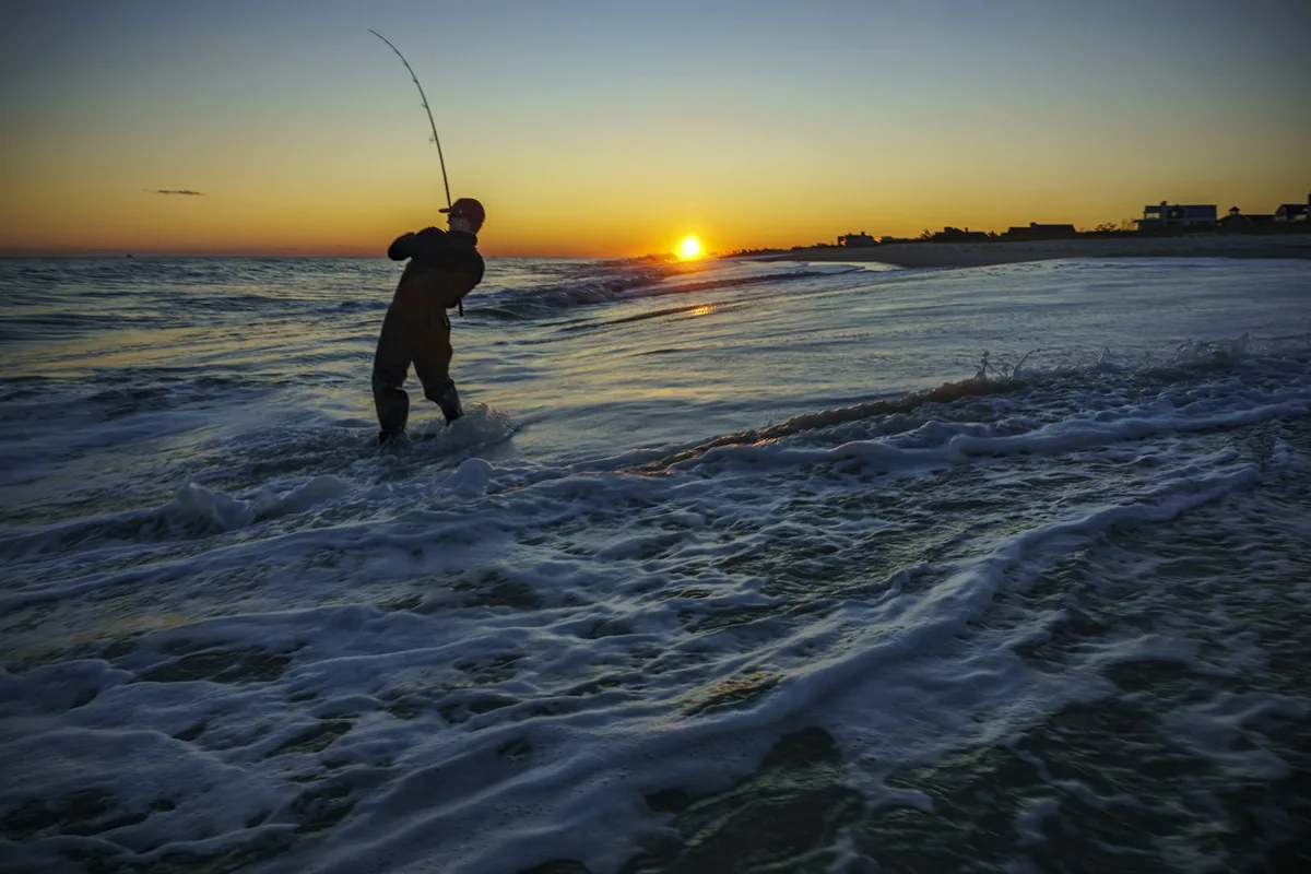Pescador de surfcasting na praia ao pôr do sol