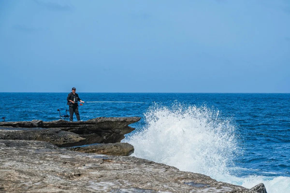 Pescador em costa rochosa com ondulação a rebentar