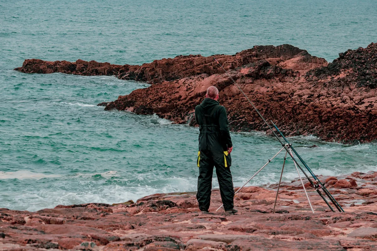 Pescador junto a uma cana de fundo apoiada na margem